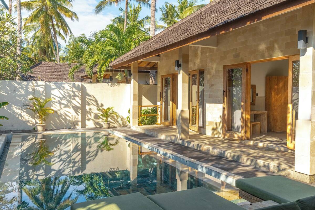 A modern poolside area with a stone building, a clear pool, and surrounding palm trees.