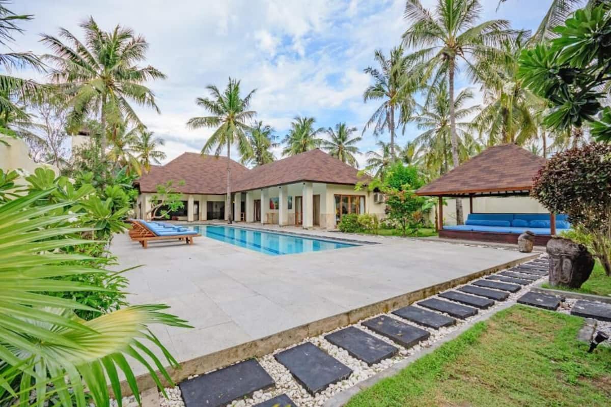 A resort with a swimming pool, palm trees, and a covered seating area.