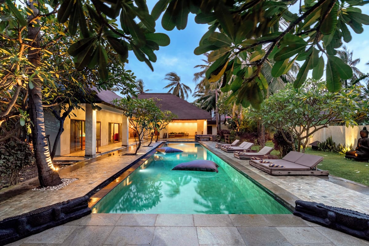 A swimming pool with lounge chairs and a well-lit house in the background.