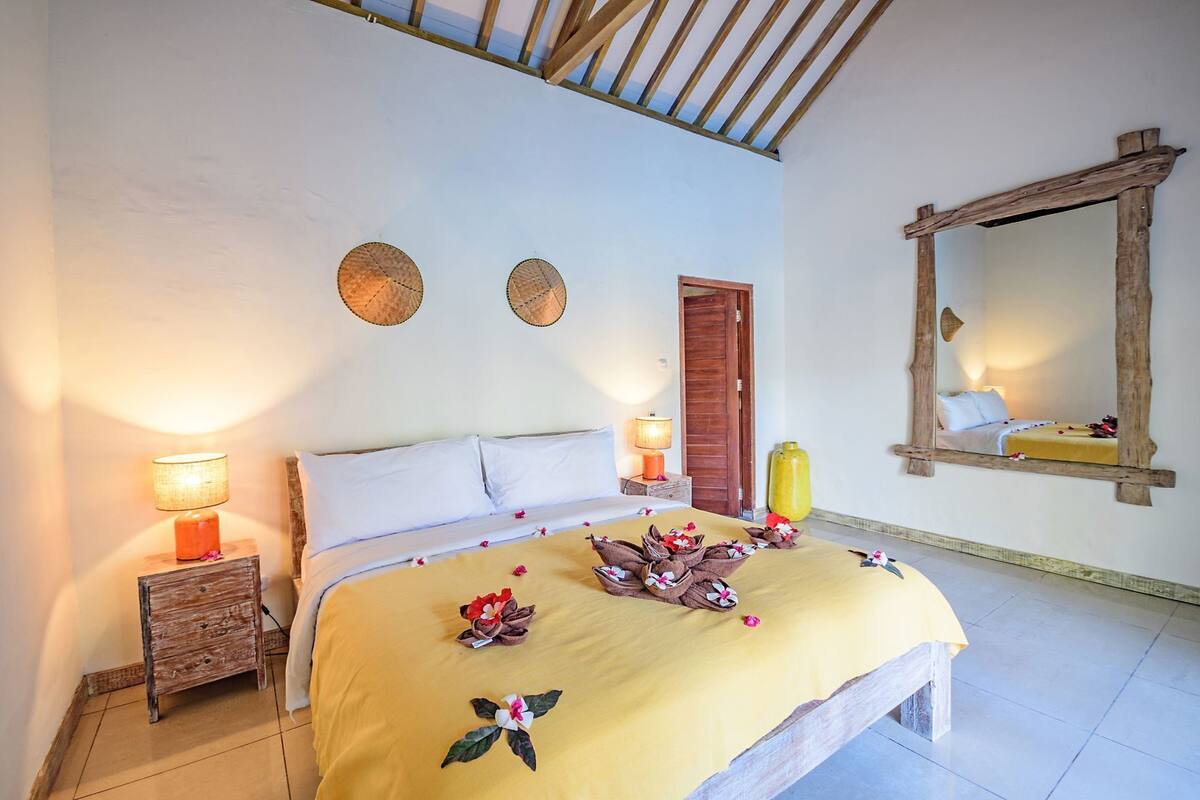 A bedroom with a bed, two bedside lamps, a wooden nightstand, a mirror, and a door.