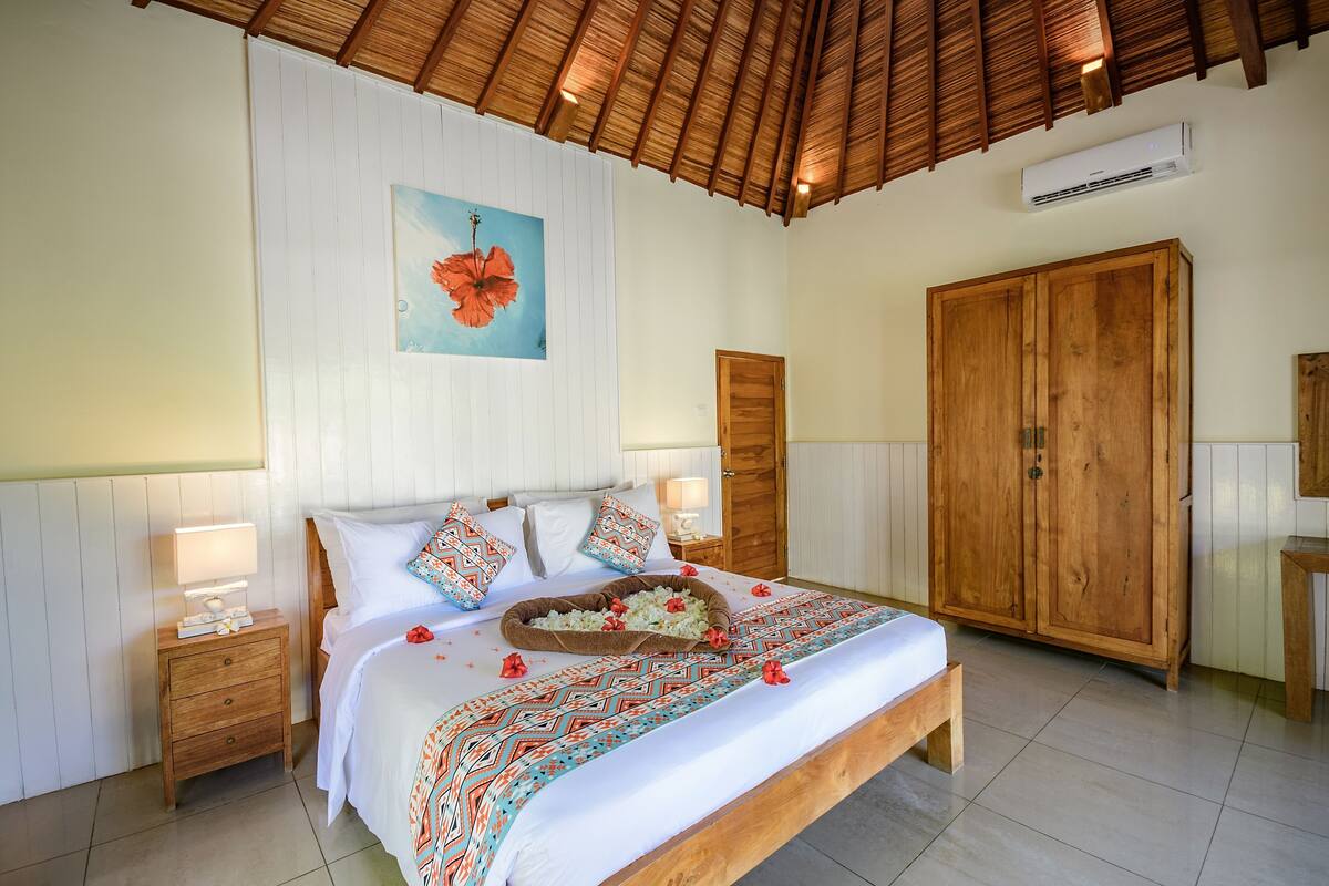 A bedroom with a bed, wooden wardrobe, bedside tables, and a ceiling fan.