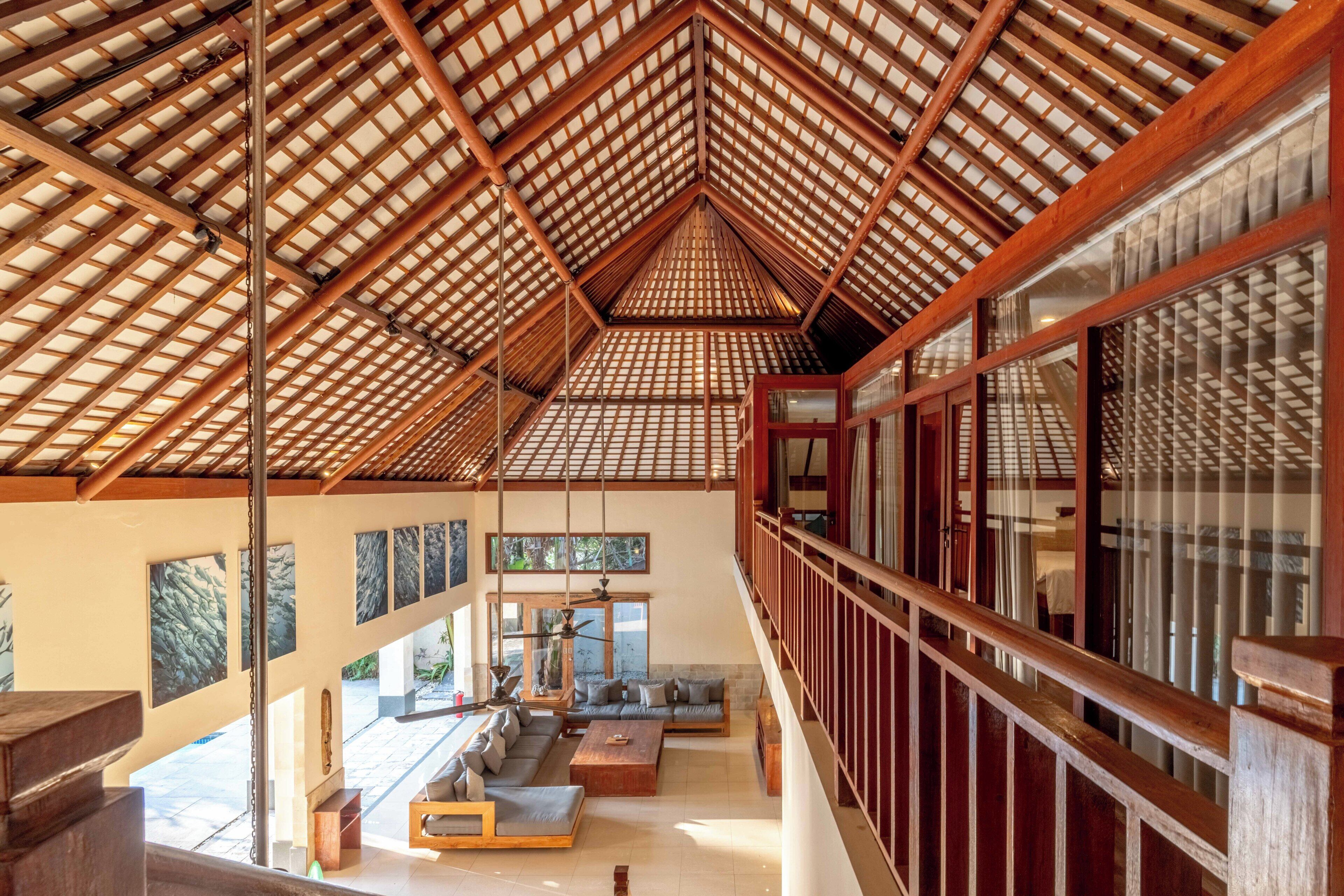 A spacious interior with a high ceiling and wooden beams, featuring a balcony with a view of the outdoors.