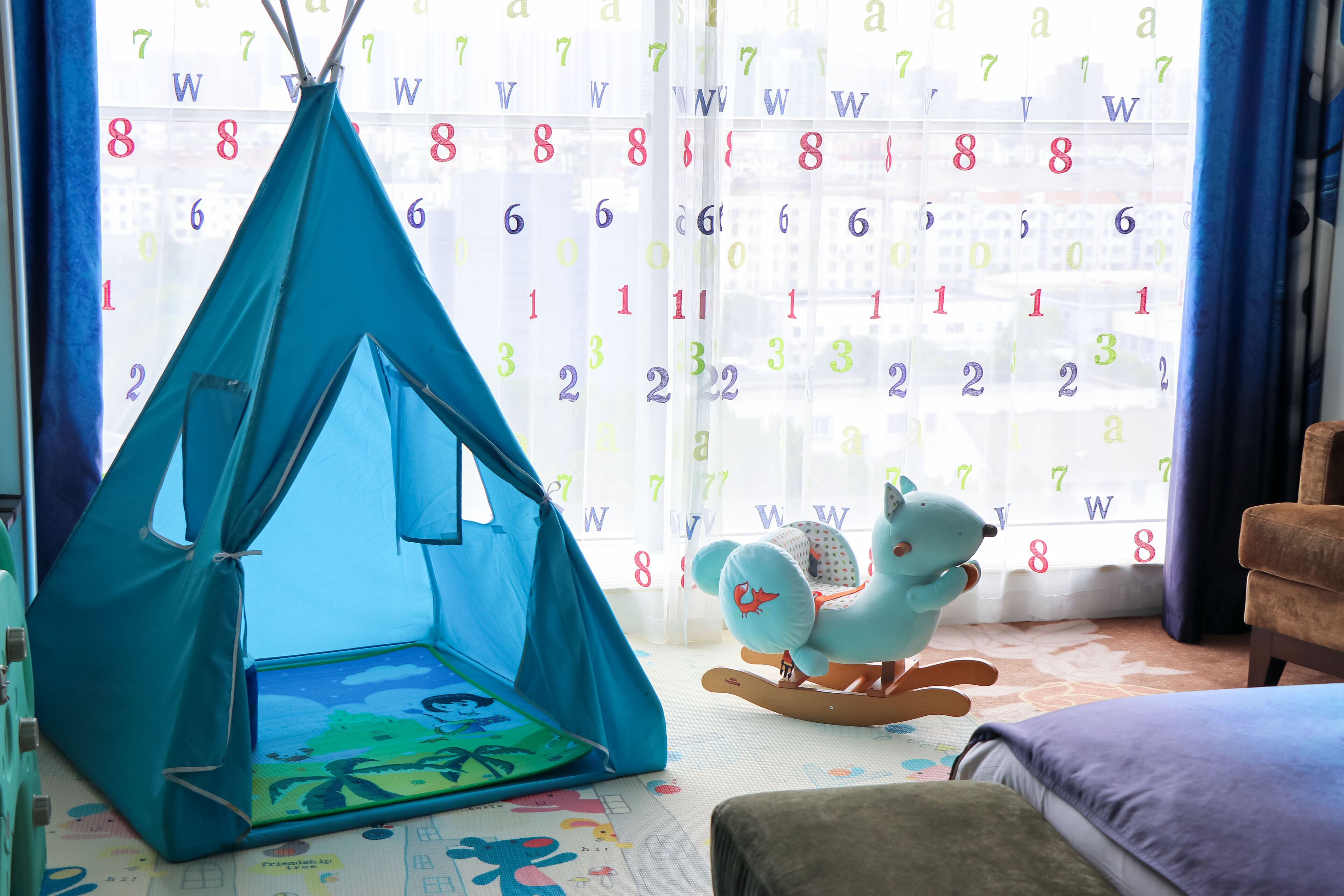 Een kamer met een blauwe tent, een schommelpaard en een kalender op het raam.