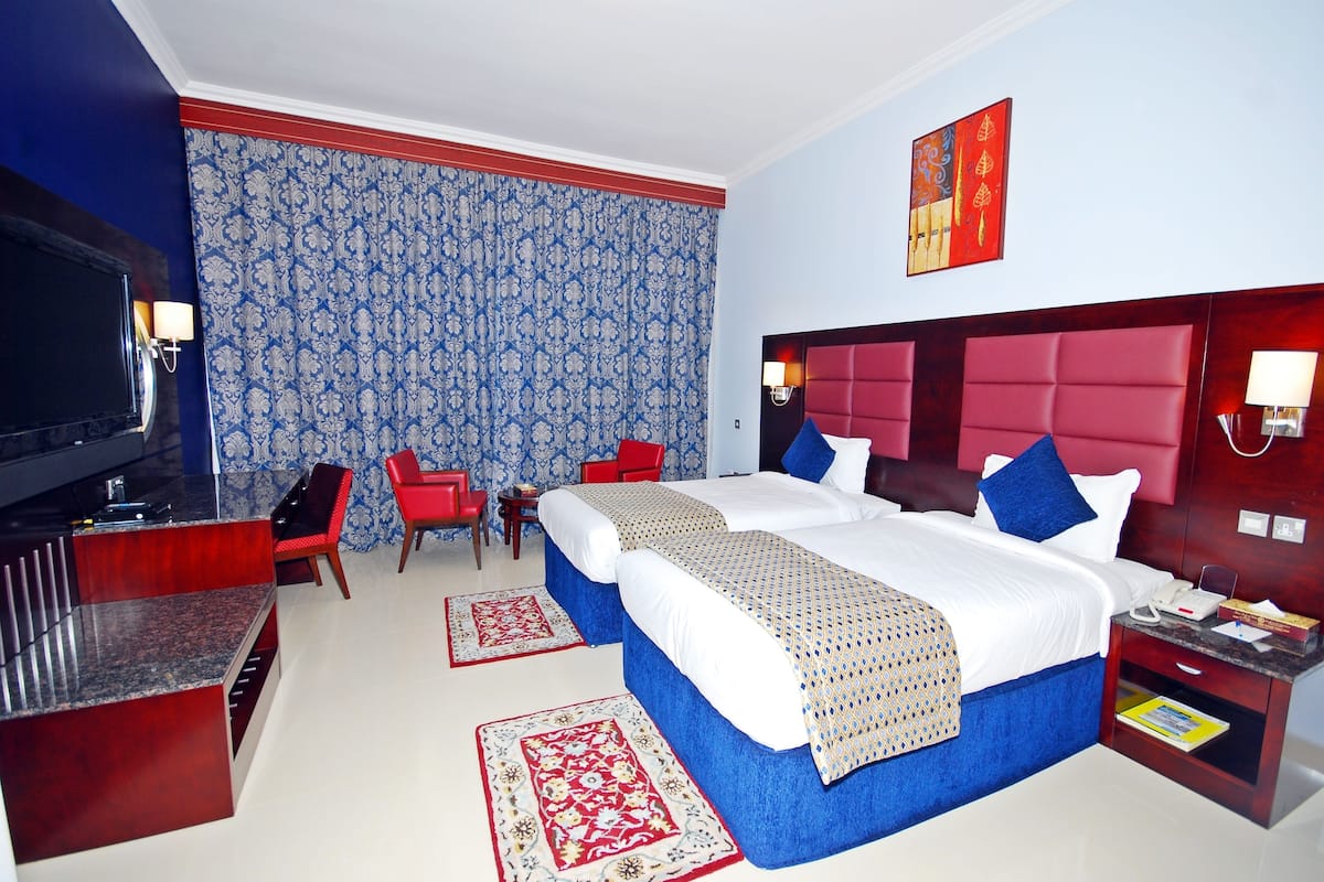 A hotel room with a large bed, two bedside tables, a TV, and a desk with a chair.