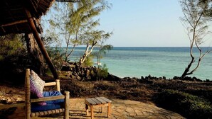 A wooden bench with a cushion and a small table on a stone patio overlooking a beach.