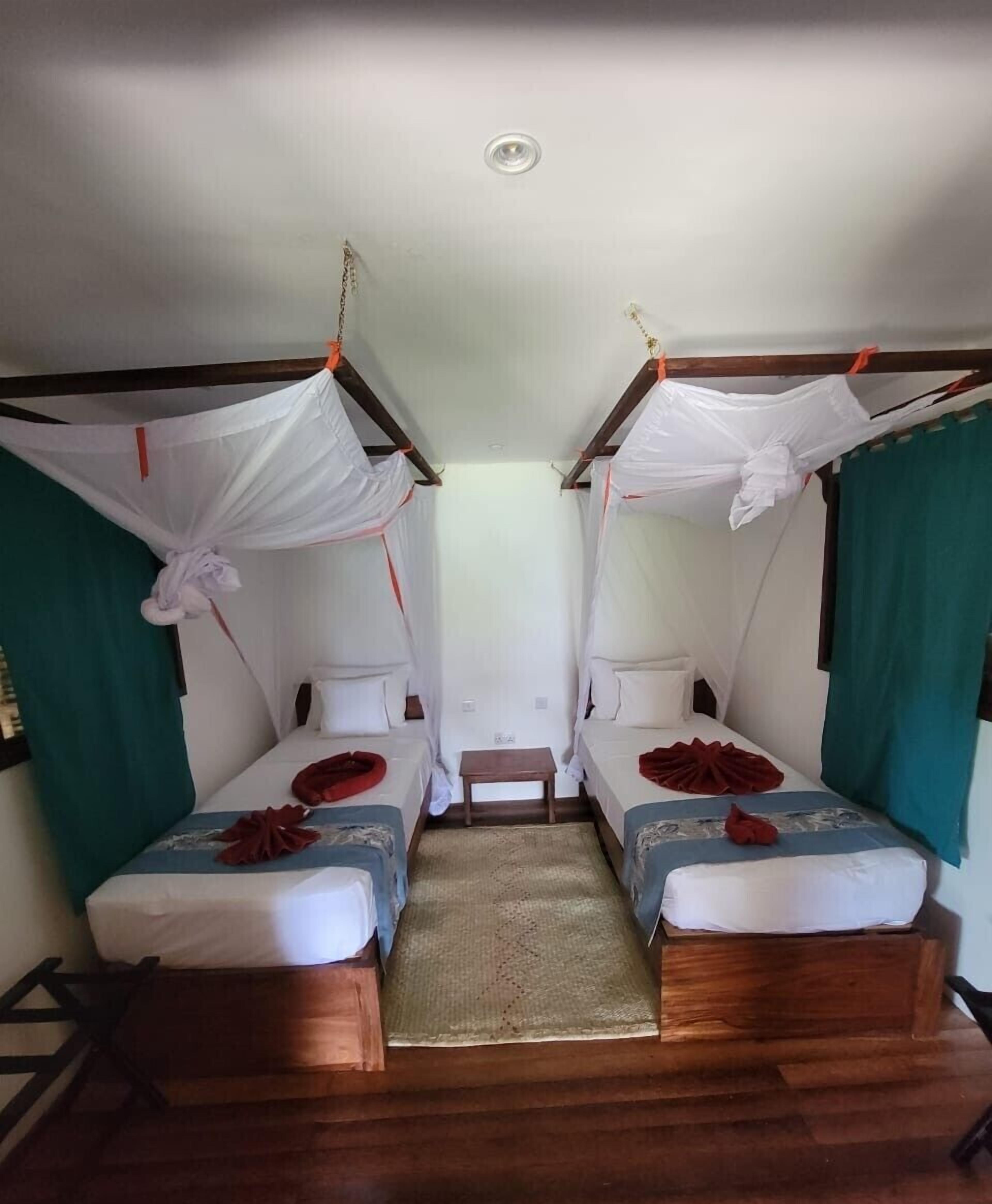 A room with two beds, each with a canopy and a small table in the center.