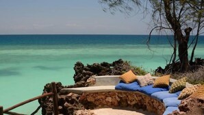 A stone bench with cushions and a view of the ocean.