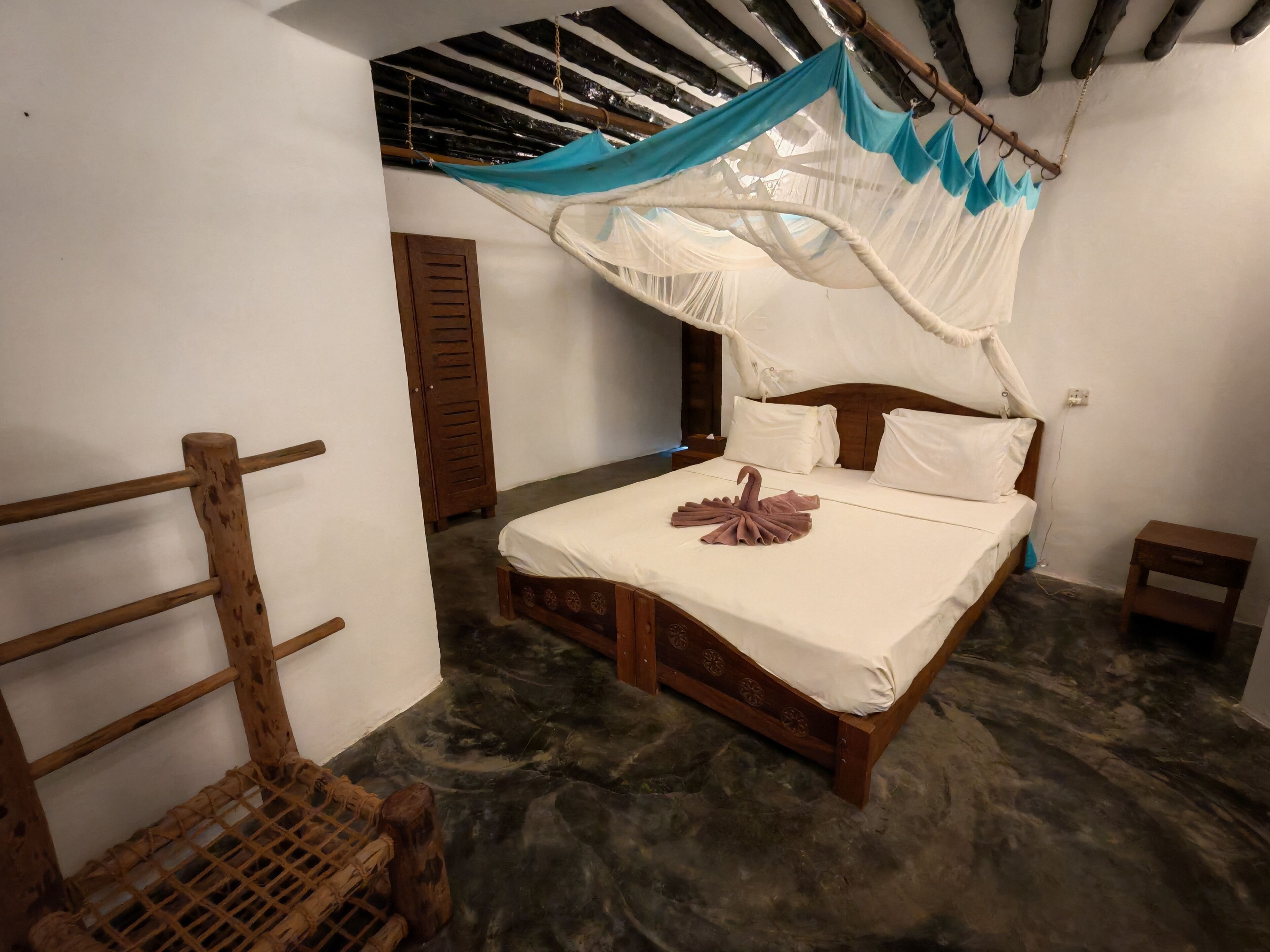 Ein Schlafzimmer mit einem hölzernen Bett, einem Moskitonetz und einem Holzstuhl.