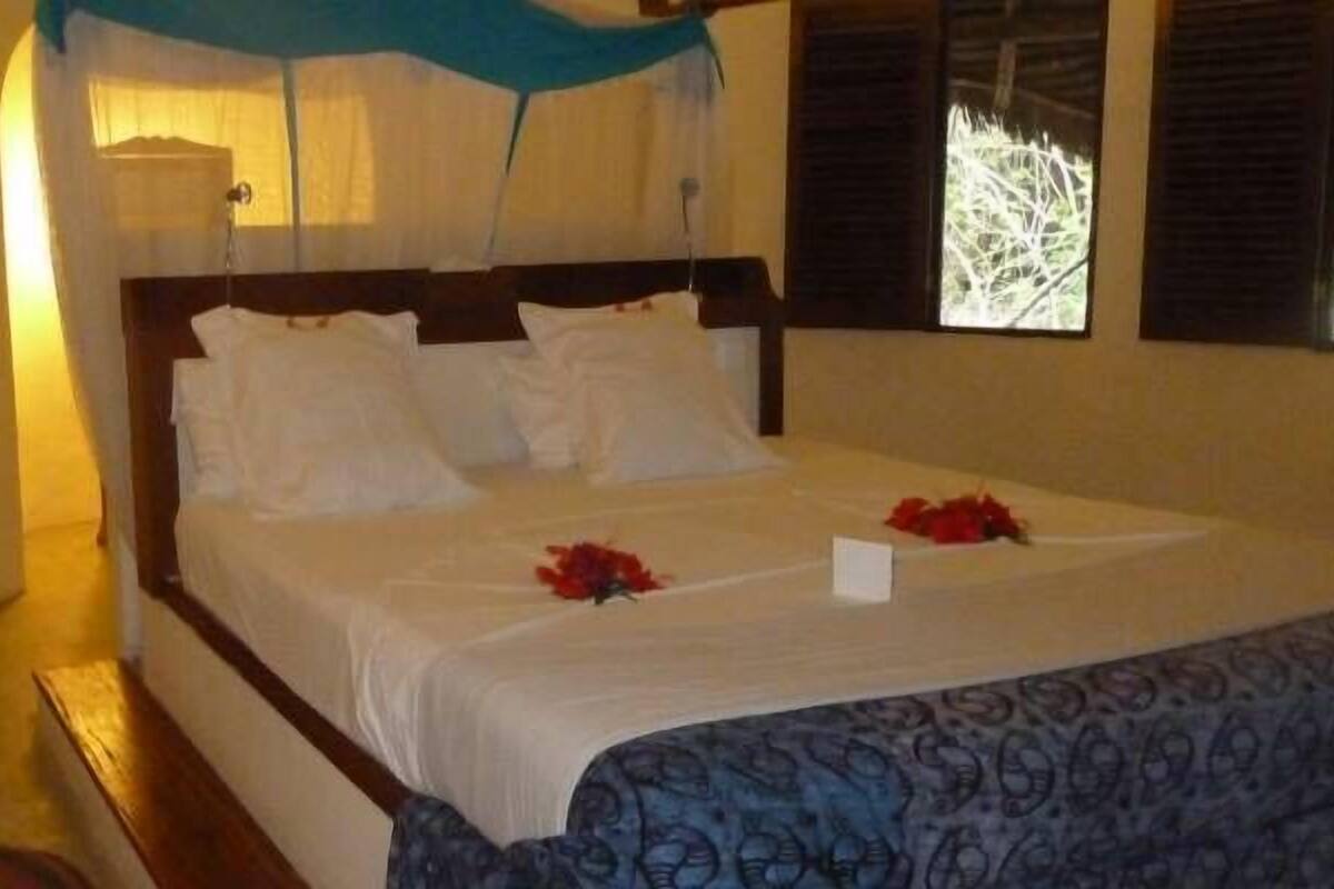 Ein Bett mit Baldachin, ein Nachttisch und ein Fenster mit Rollläden.