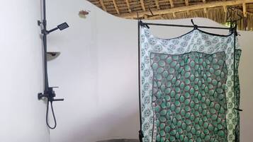 A room with a thatched roof, a shower area with a patterned curtain, and a white wall with a black faucet.
