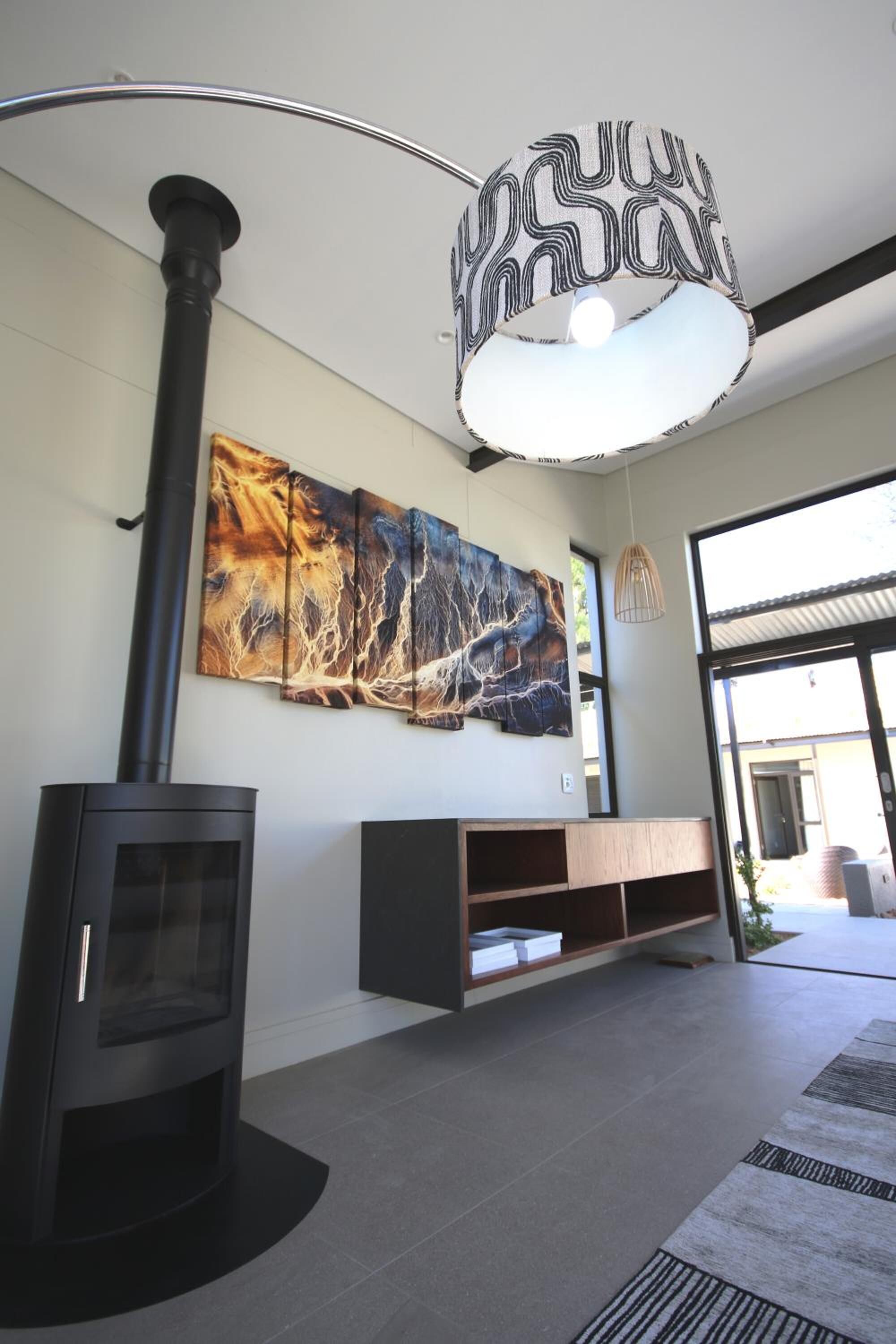 A modern living room with a black wood-burning stove, a large abstract painting, and a contemporary light fixture.