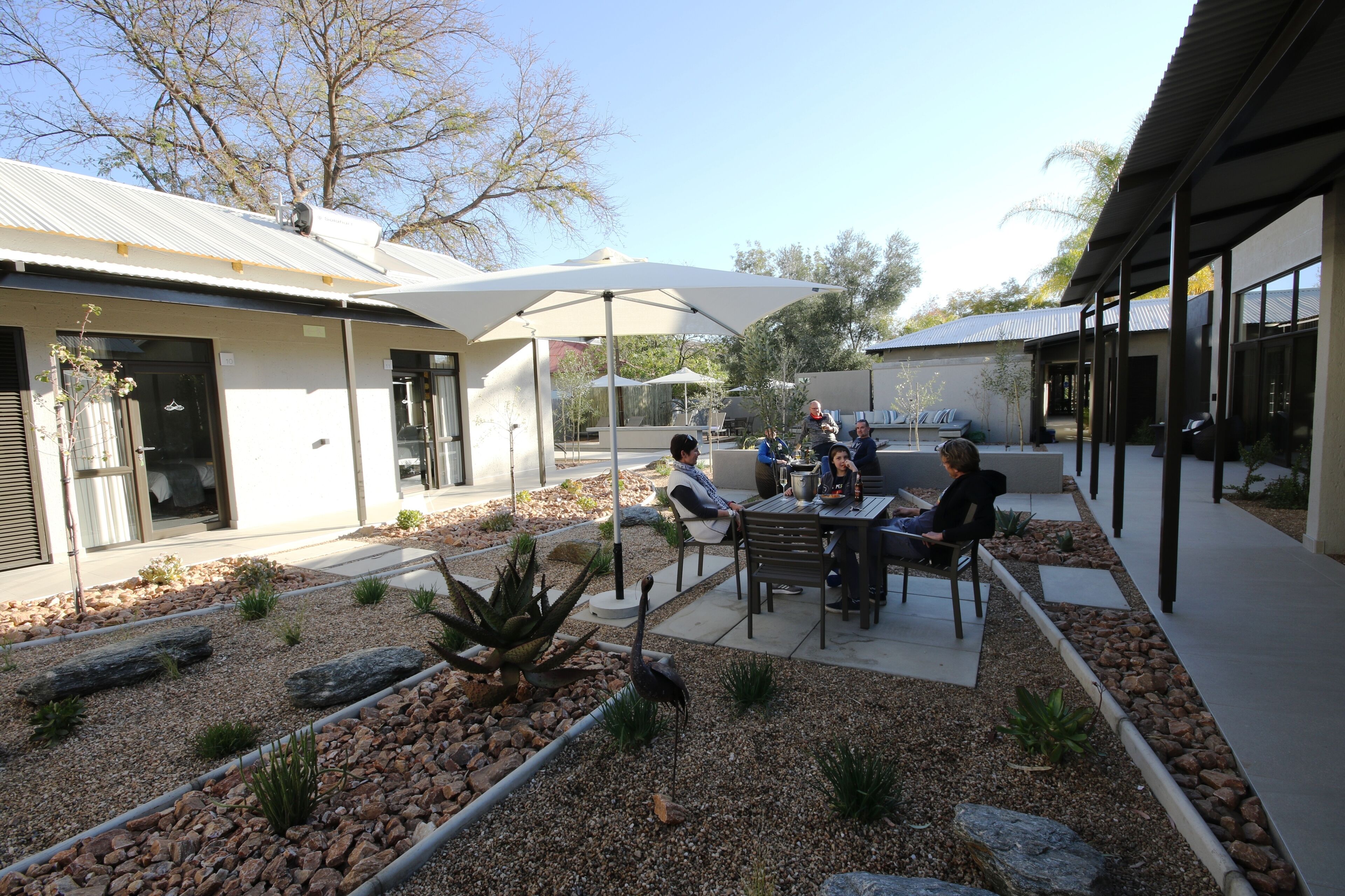 An outdoor patio area with tables and chairs, surrounded by a landscaped garden with rocks and plants.