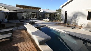 A modern outdoor pool area with a wooden deck, lounge chairs, and umbrellas. - The Elegant Guesthouse (Windhoek)