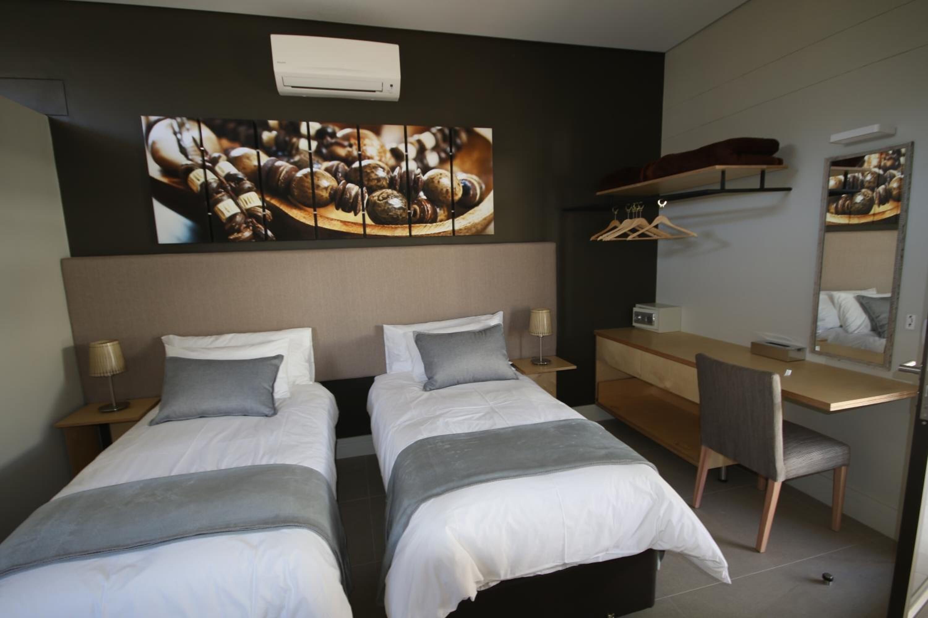 Habitación de hotel con dos camas, un escritorio, una silla, un armario y un espejo grande.