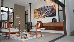 A modern interior with a fireplace, two wooden chairs, a bench, and a large abstract painting on the wall. - The Elegant Guesthouse (Windhoek)