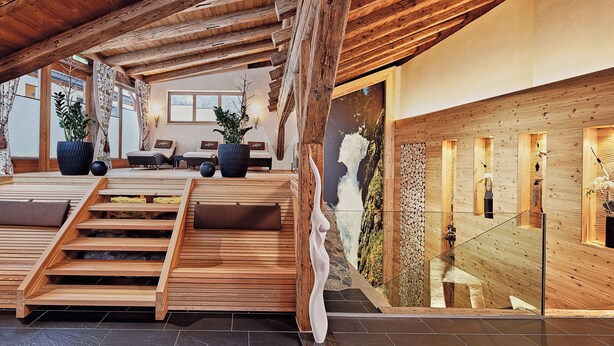 A spacious indoor area with wooden beams, a stone wall, and a wooden staircase. - Hotel Traube (Pfunds)