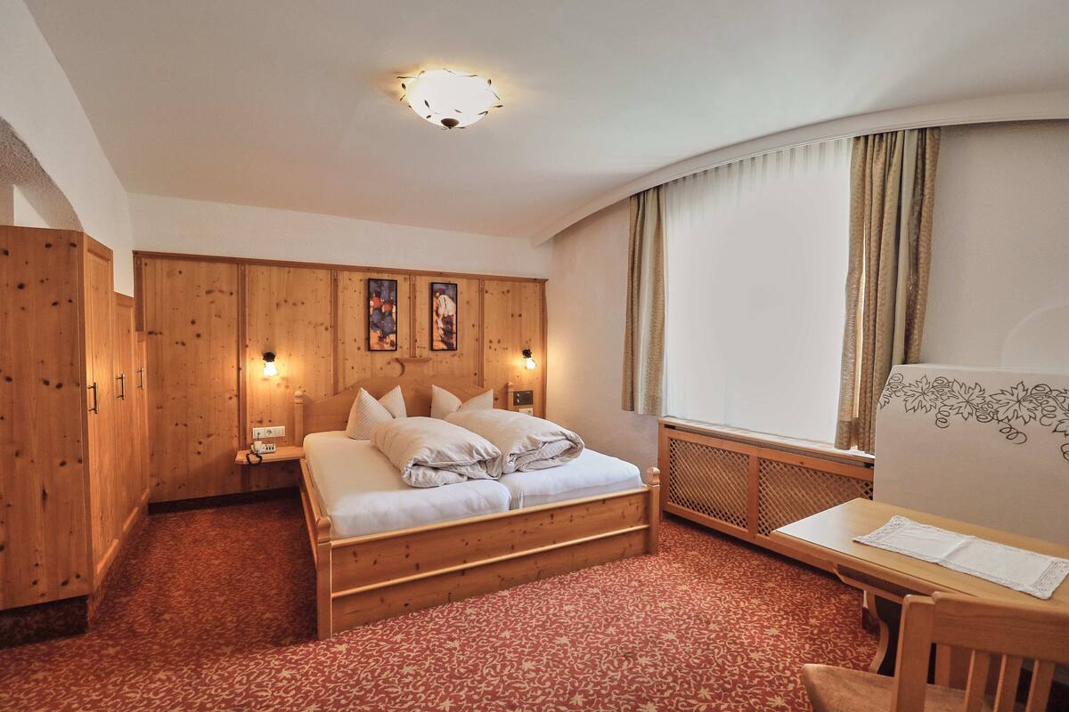 Une chambre d’hôtel avec un lit en bois, un bureau et une fenêtre avec des rideaux.