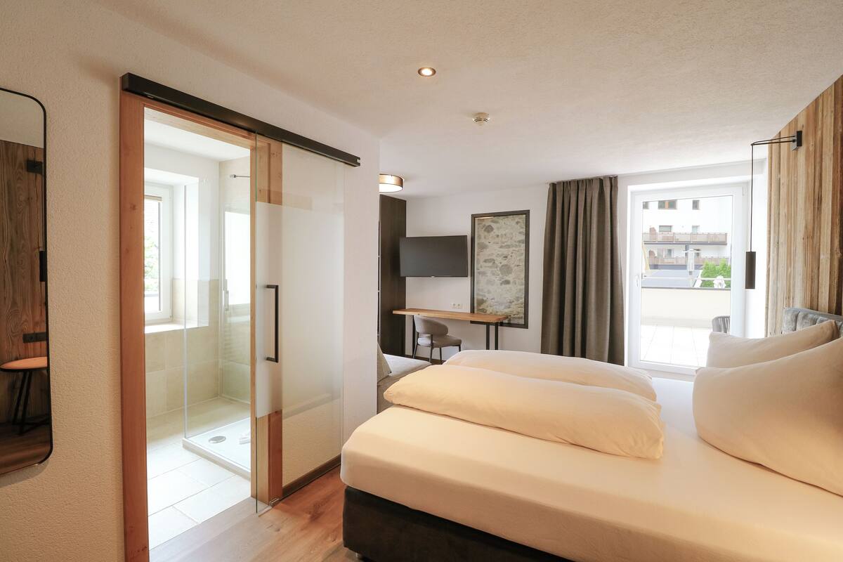 Une chambre d’hôtel moderne dotée d’un grand lit, d’un bureau, d’une télévision et d’une douche en verre.