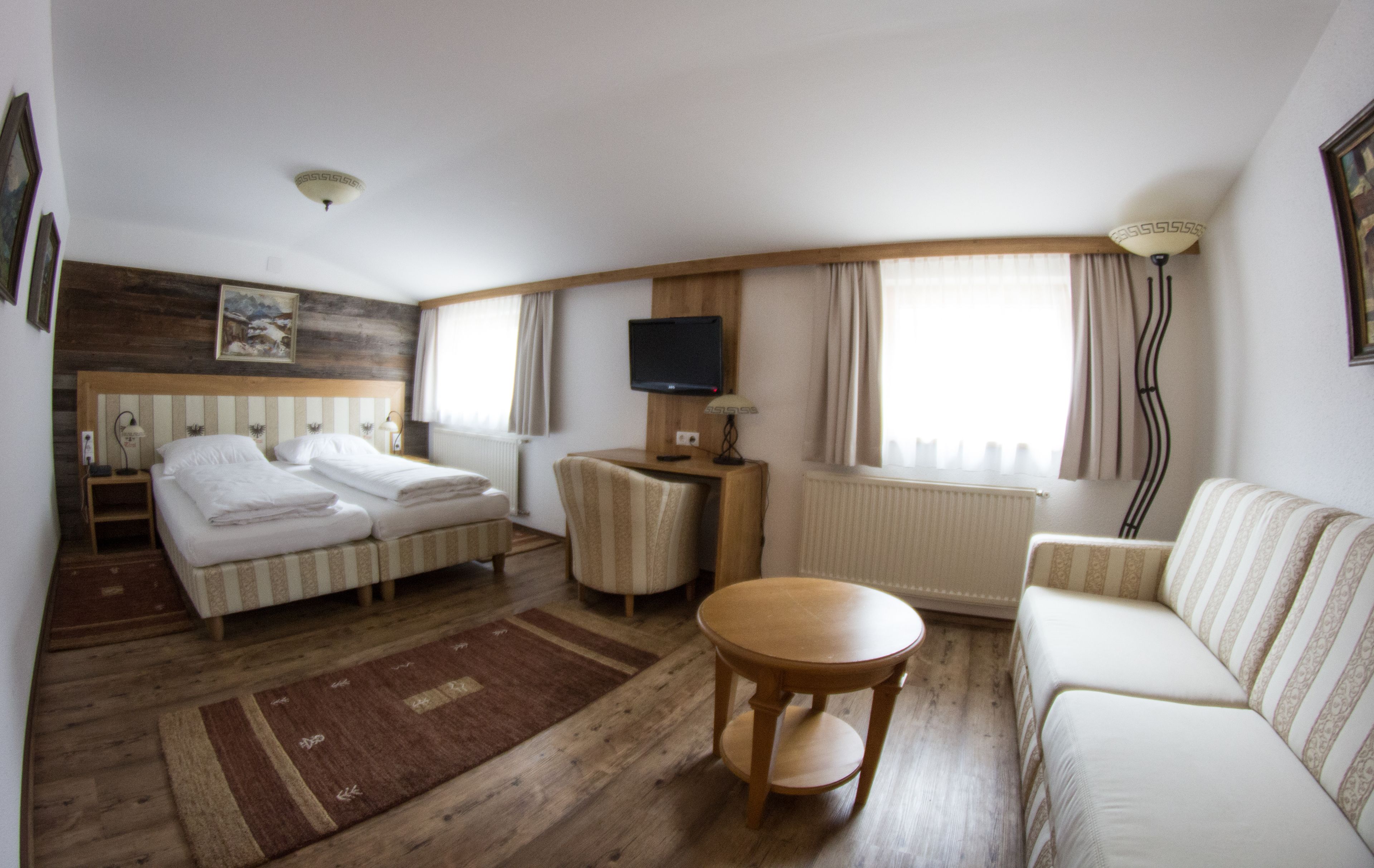 A hotel room with a bed, a sofa, a small table, a TV, and a window with curtains.