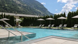 A swimming pool with lounge chairs and umbrellas, surrounded by a mountainous landscape. - Hotel Traube (Pfunds)