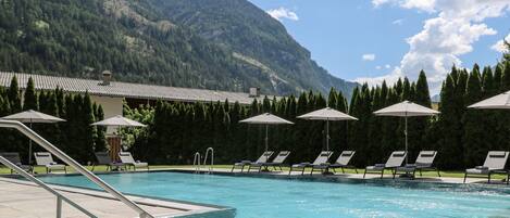 Una piscina con sillones de descanso y sombrillas, rodeada por un paisaje montañoso.