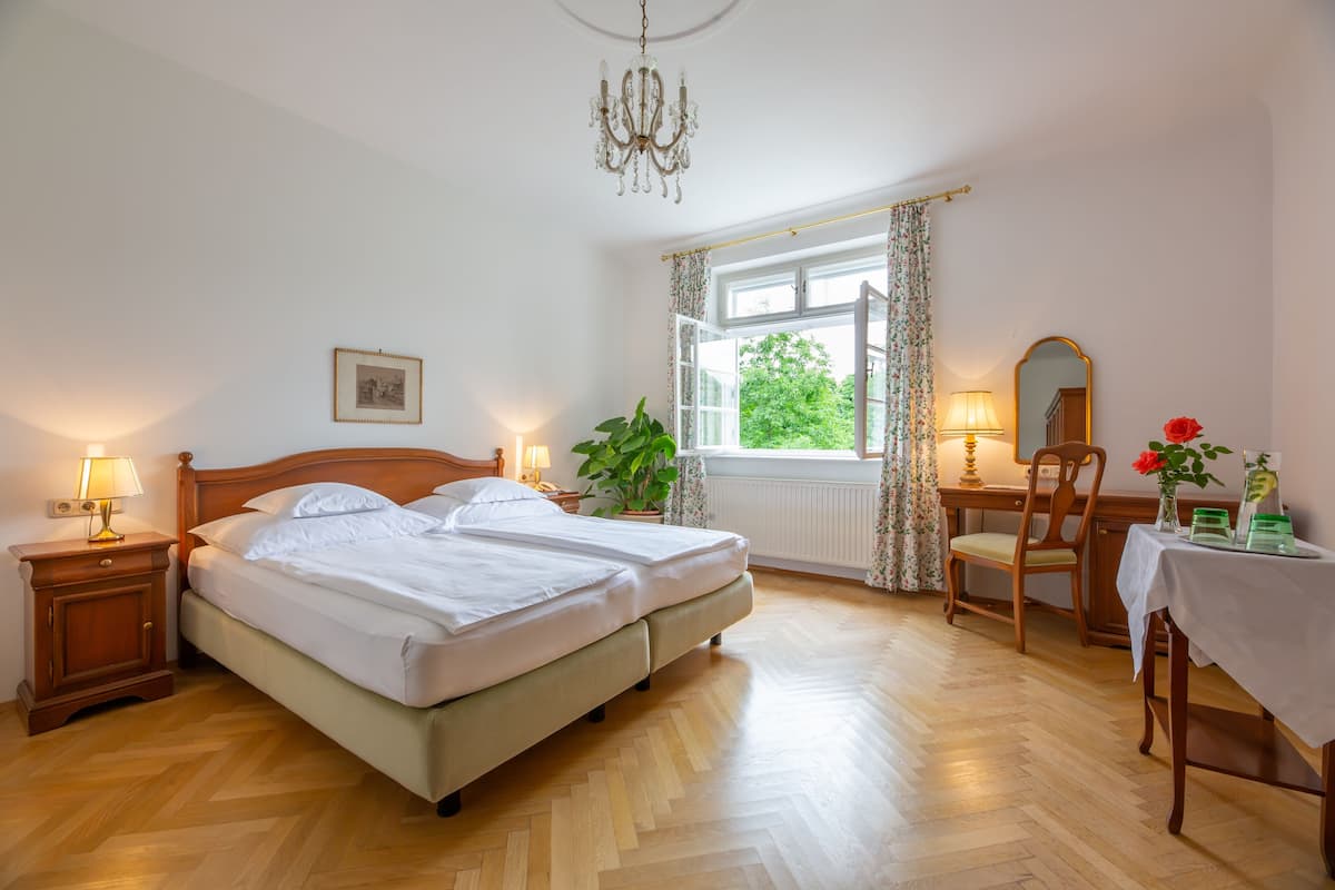 A bedroom with two beds, a desk, a chair, a mirror, and a window with curtains.