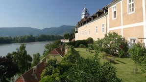 A large building with a river in the background, surrounded by greenery and a clear sky. - Richard Löwenherz (Durnstein)