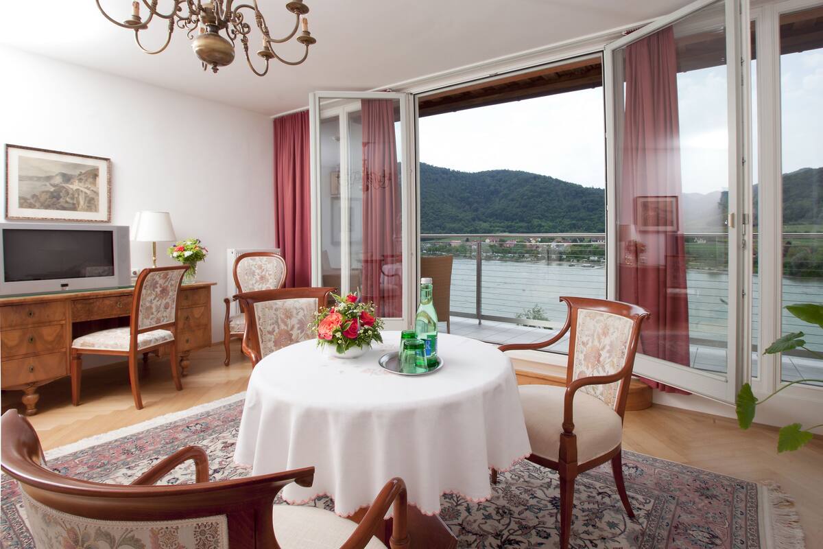 A dining area with a round table, chairs, a TV, and a view of a lake.