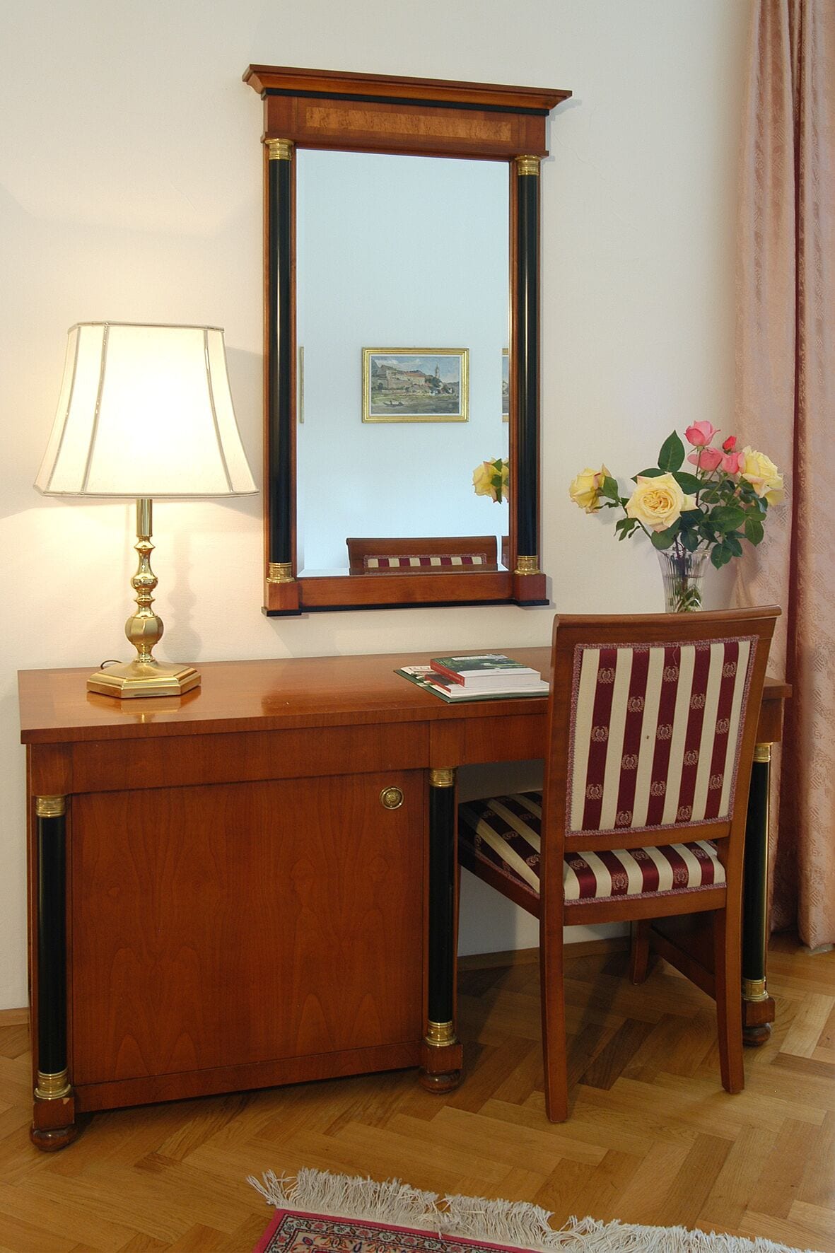 Un bureau en bois, une lampe, un miroir, une chaise et un vase avec des fleurs.