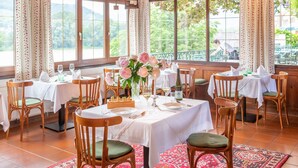 A dining area with wooden tables and chairs, floral centerpieces, and large windows with curtains. - Richard Löwenherz (Durnstein)