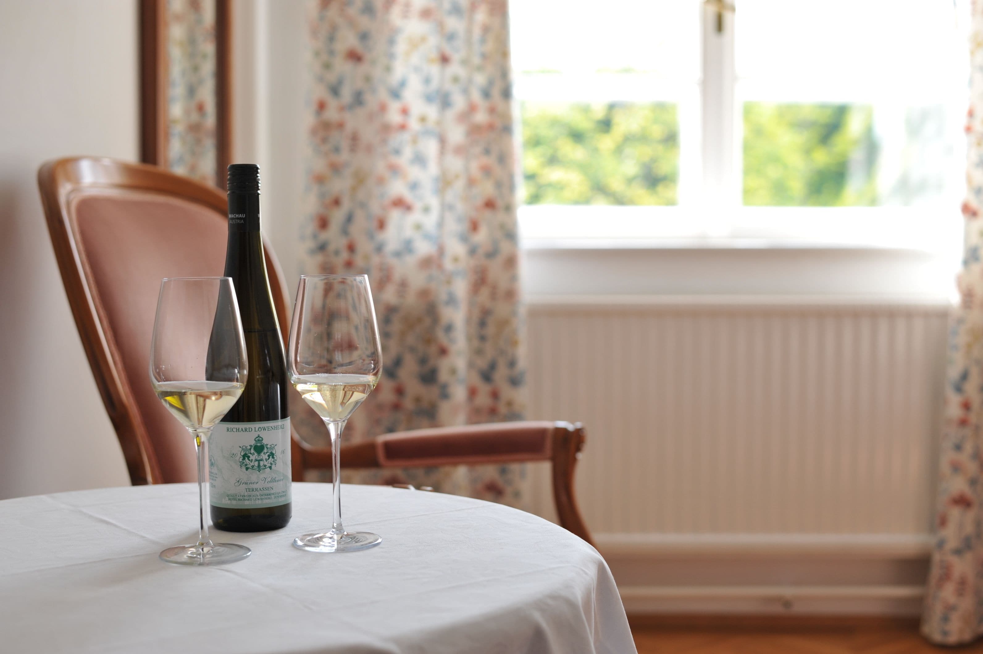 A table with a bottle of wine and two glasses on a white tablecloth.