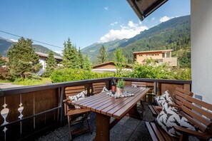 Ein Holztisch und Bänke auf einem Balkon mit Blick auf die Berge.