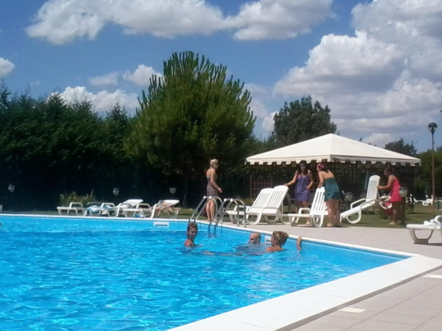 A swimming pool with lounge chairs and a covered area.
