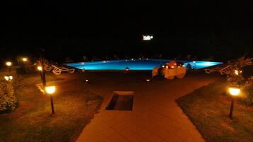 Vista nocturna de una piscina con sillones de descanso y una mesa preparada para un evento.