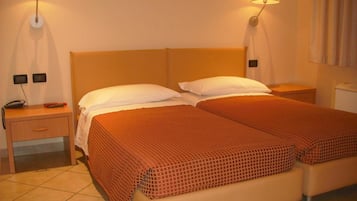 Habitación de hotel con dos camas, cada una con una colcha estampada roja, un cabecero de madera y dos lámparas de pared. Hay una mesita de noche con un teléfono y un objeto rojo encima.