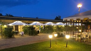 An outdoor seating area with umbrellas and tables, surrounded by greenery and a building with a tiled roof. - KoKo Hotel Milano Marittima (Ravenna)