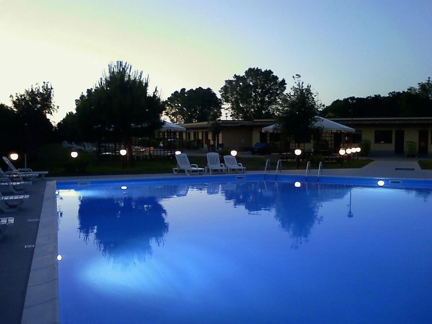 Una piscina amb gandules i ombrel·les, envoltada d'arbres i edificis.