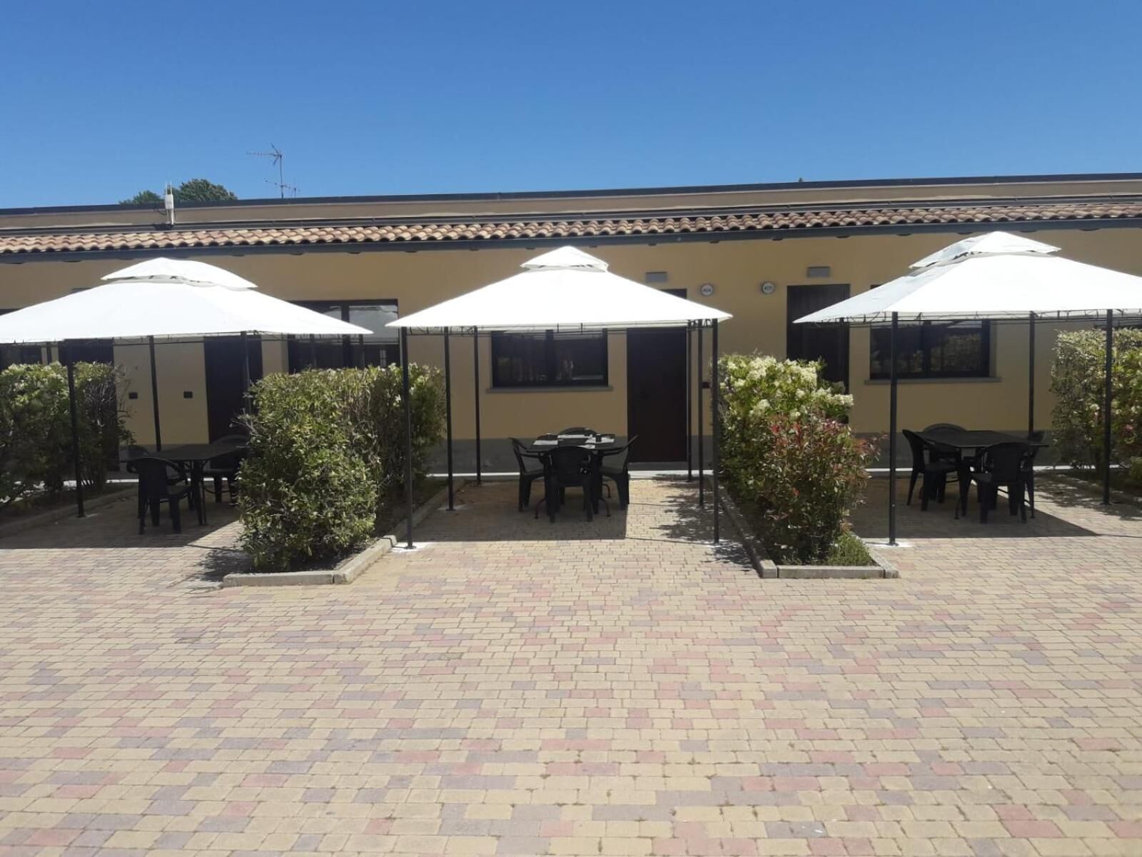 Un patio con mobiliario exterior bajo sombrillas, suelo de baldosas y un edificio con techo de tejas al fondo.