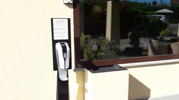 A reception area with a sign indicating the direction to the reception, a hand sanitizer dispenser, and a window reflecting the hotel name and logo.