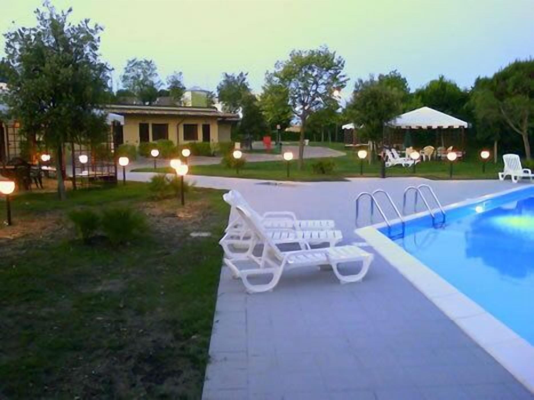 Piscina com cadeiras de descanso e um edifício ao fundo.