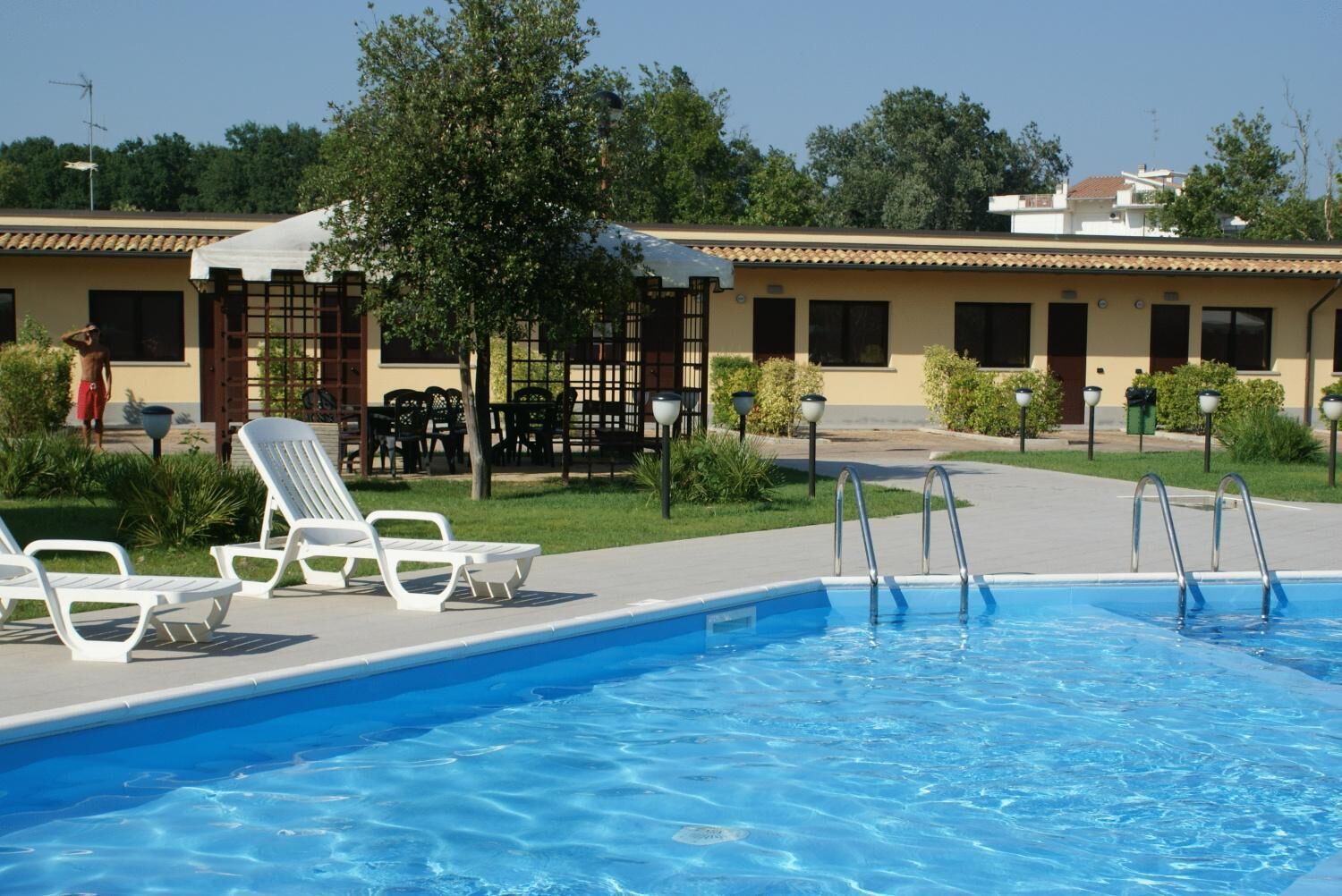 Ein Schwimmbecken mit Liegestühlen und einer überdachten Terrasse.
