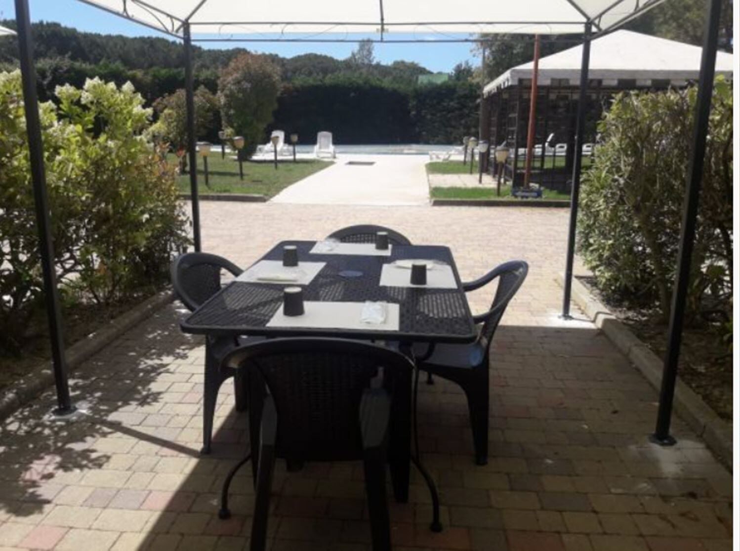Une terrasse extérieure avec une table et des chaises, entourée de verdure et un chemin menant à un bâtiment.