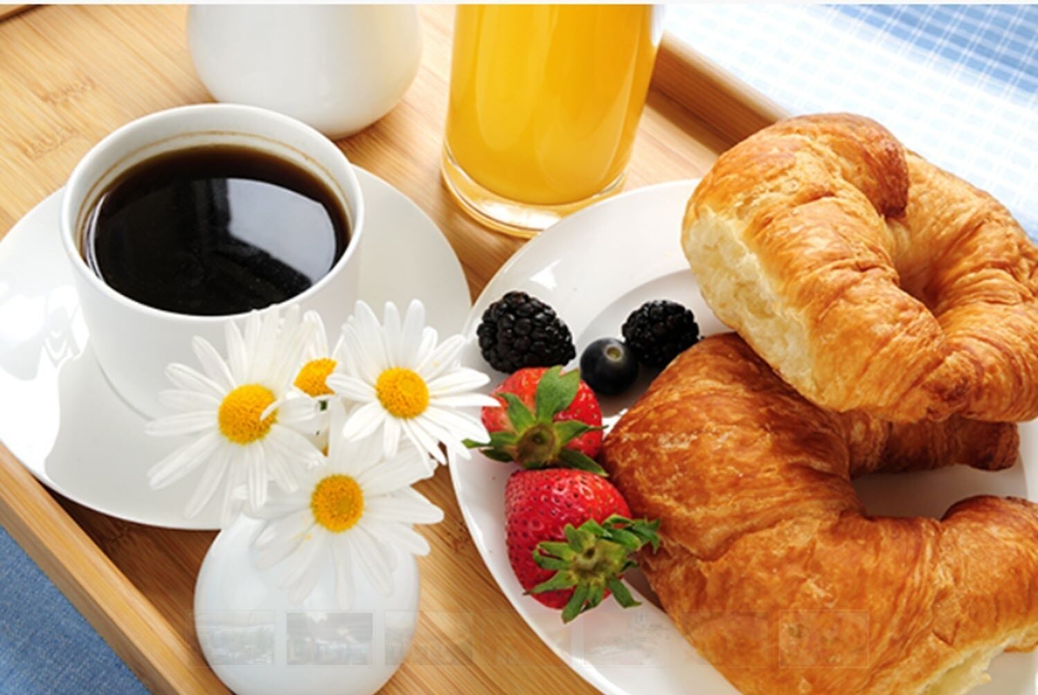 A breakfast tray with croissants, strawberries, blackberries, a glass of orange juice, and a cup of coffee.