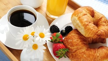 Bandeja de desayuno con cruasanes, fresas, zarzamoras, un vaso de jugo de naranja y una taza de café.