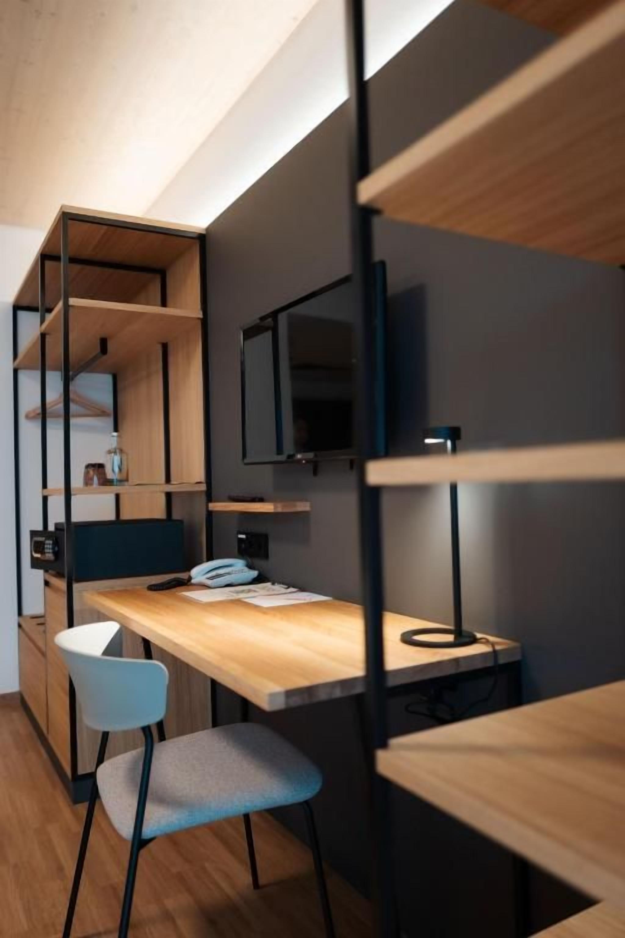 Una habitación moderna con un escritorio de madera, una silla, televisor y estanterías empotradas.