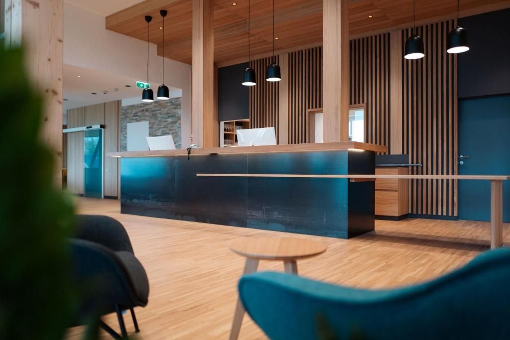 Un espace d’accueil moderne avec un comptoir de réception en bois, des luminaires suspendus et une vue sur la cuisine en arrière-plan.