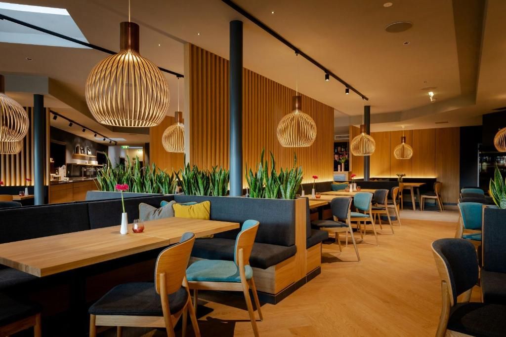 Un intérieur de restaurant moderne, caractérisé par de hauts plafonds, des luminaires suspendus et une variété d’aménagements, notamment des banquettes et des tables.