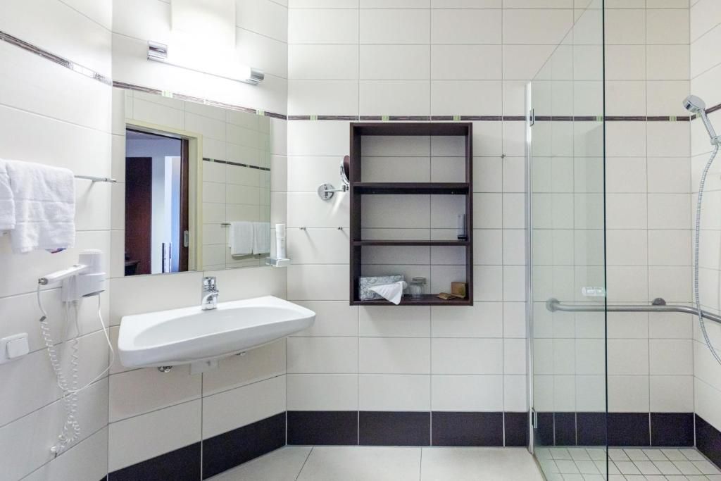 Un baño con lavamanos blanco, espejo, cabina de ducha de vidrio y una estantería.