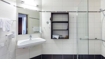 Un baño con lavamanos blanco, espejo, cabina de ducha de vidrio y una estantería.