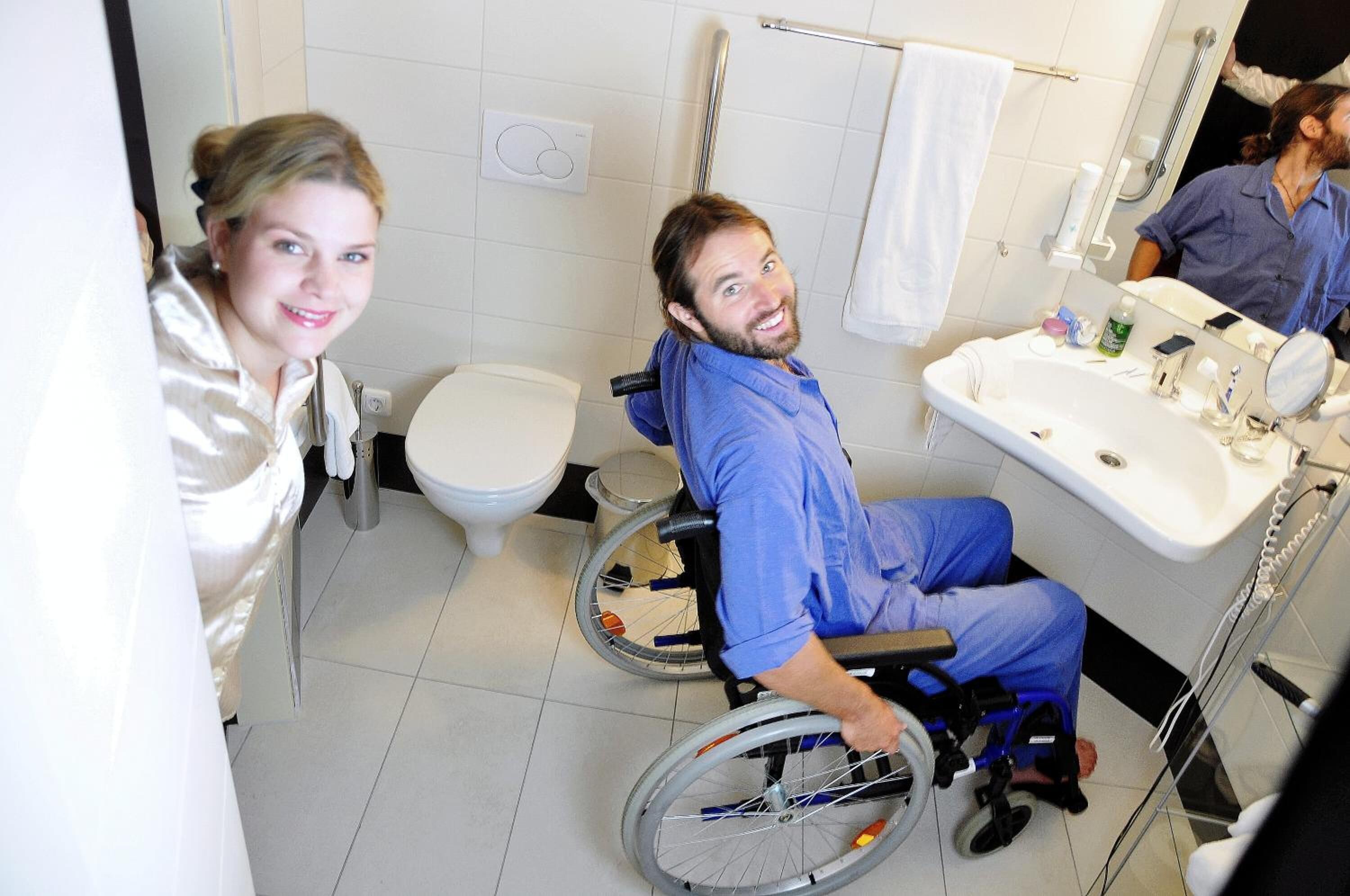 A wheelchair-accessible bathroom with a toilet, sink, and mirror.